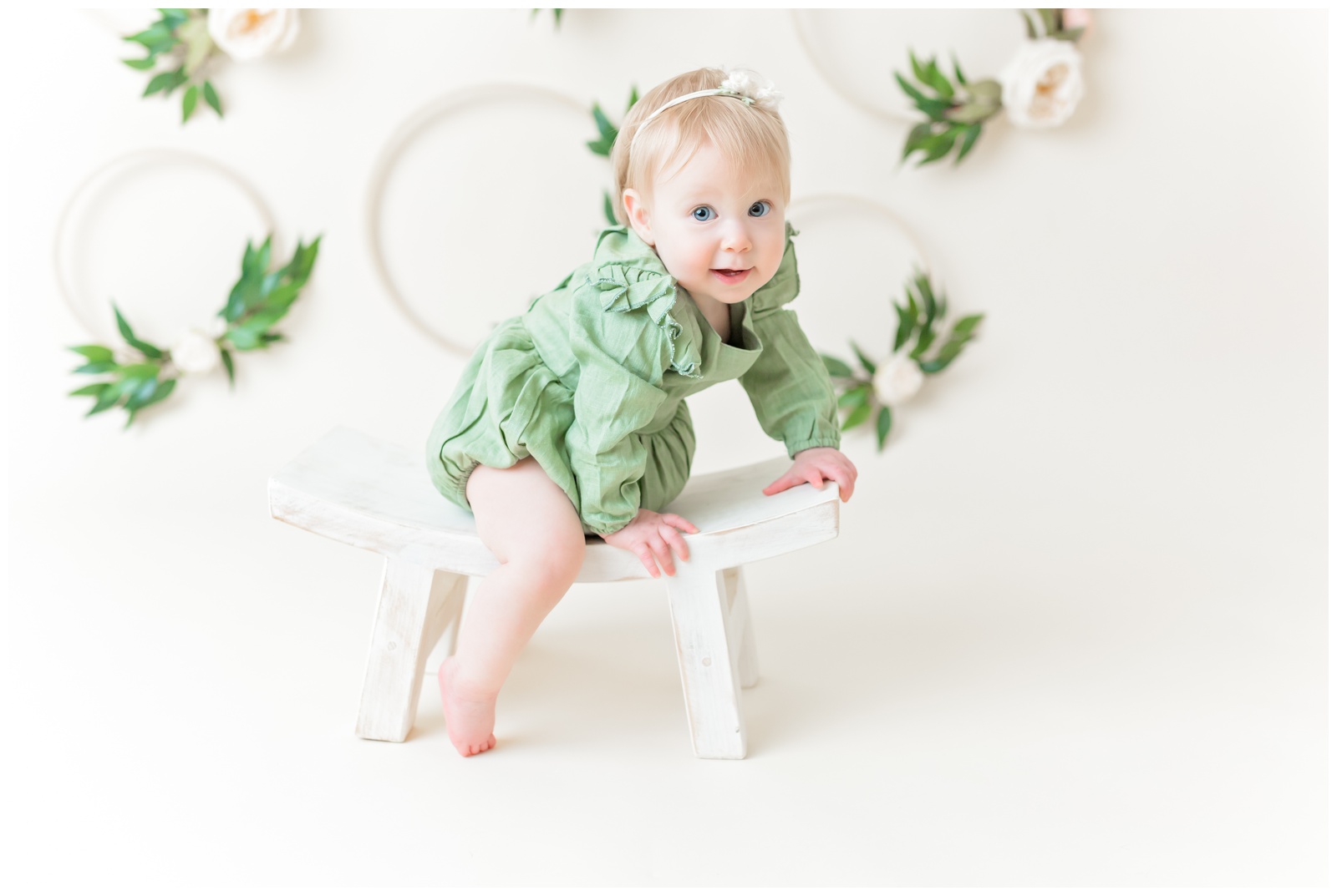 1 year old in green romper on stool, studio session, organic floral hoops in background