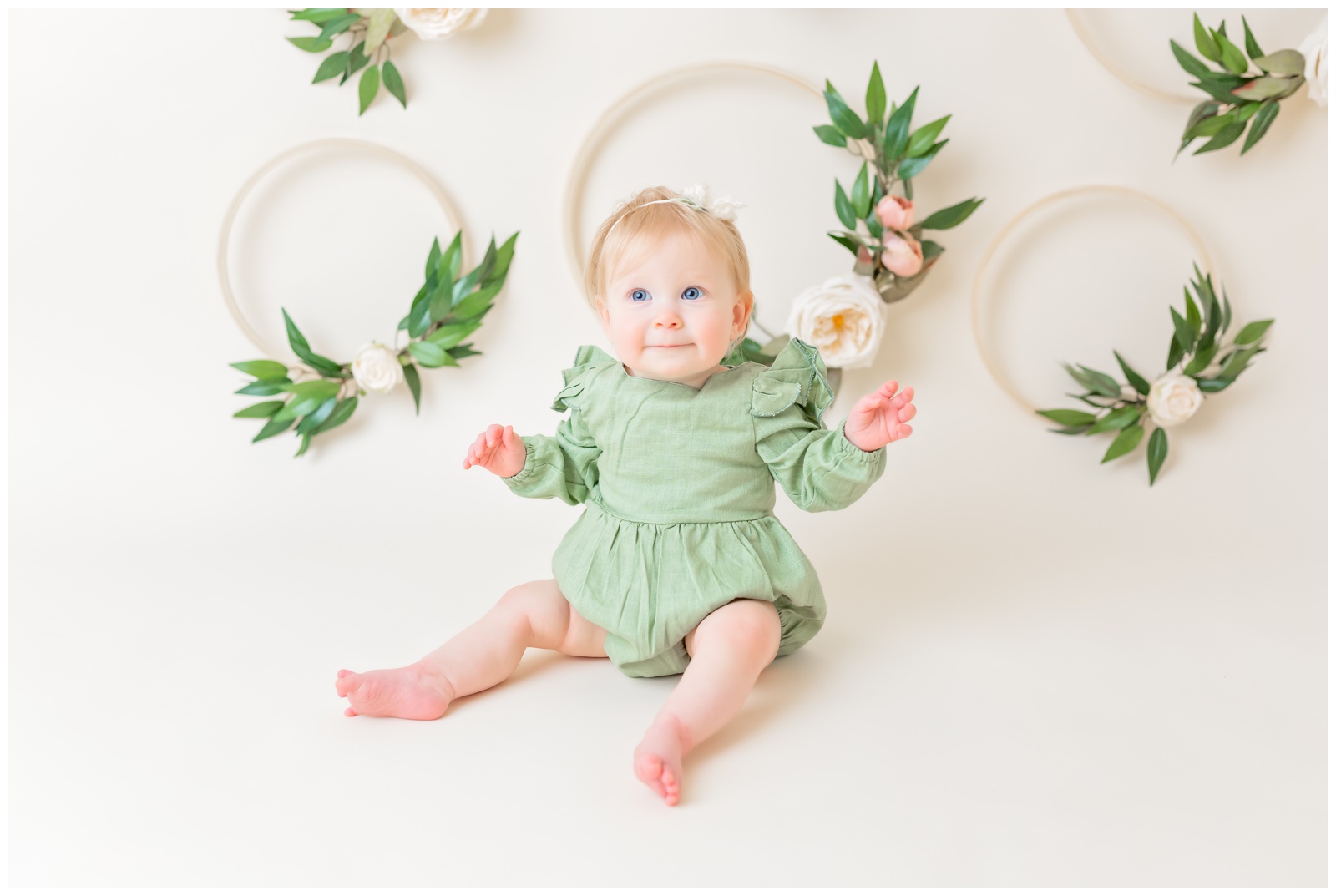 1 year old in green romper with hands outstretched, cake smash session, organic floral hoops in background